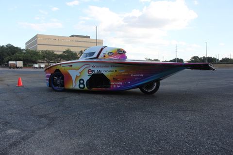 Low, wide solar car with a multicolor livery parked on asphalt
