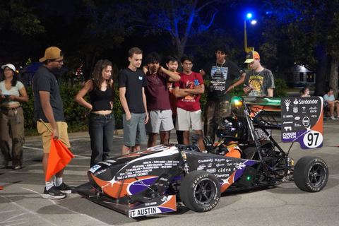 Low, wide solar car with a multicolor livery parked on asphalt