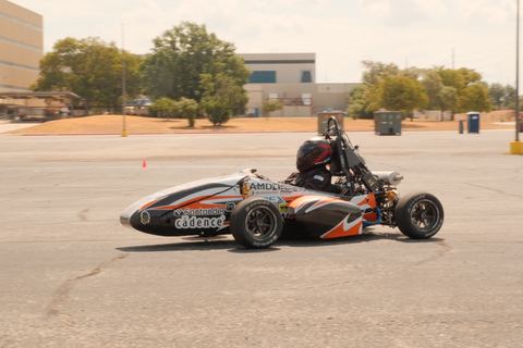 The Combustion team’s open-wheel race car with orange and black livery and a helmeted driver