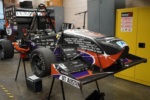Low, wide solar car with a multicolor livery parked on asphalt